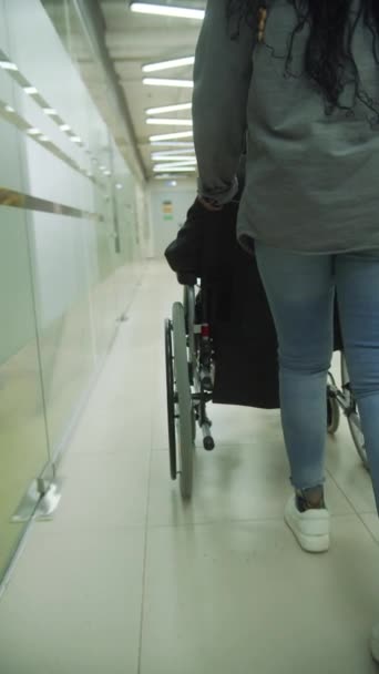 En ung dam kör sin kollega i rullstol genom kontoret — Stockvideo