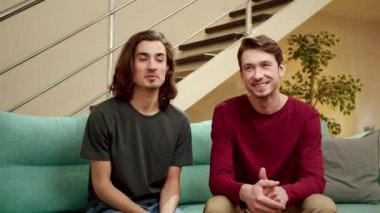 İki dost canlısı adam konuşuyor ve kameraya bakıyor.