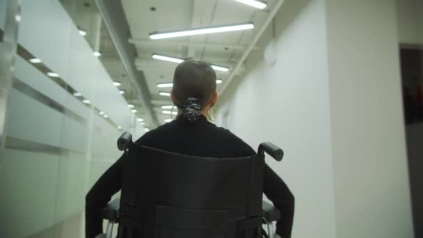 Seorang wanita muda naik kursi roda melalui kantor — Stok Video