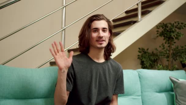 Een jongeman zwaait met zijn hand en praat voor de camera. — Stockvideo