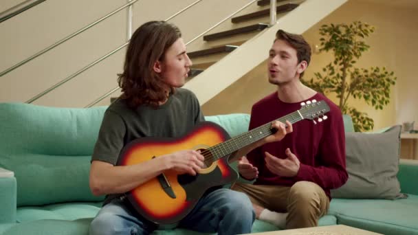 En ung man spelar gitarr för sin vän och båda sjunger. — Stockvideo
