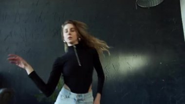 Doğal sarı saçlı genç bir kadın koridorda coşkuyla dans ediyor.