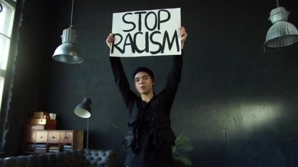 Stop rasizmowi azjatycki aktywista trzyma plakat w pokoju z czarną ścianą — Wideo stockowe