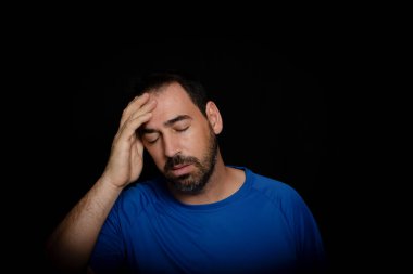 Mavi tişörtlü sakallı adam siyah arka planda poz veriyor. Moda konsepti