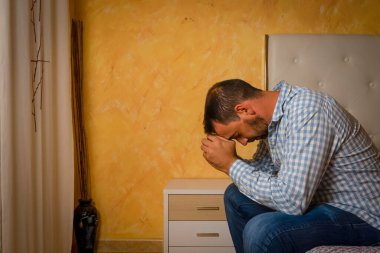 Çekici sakallı adam evdeki yatak odasında üzgün ve üzgün. 30-40 yaş arası dramatik bir hayat tarzı portresi, yatakta oturan yakışıklı bir adam, endişeli ve çaresiz. Depresyon kavramı