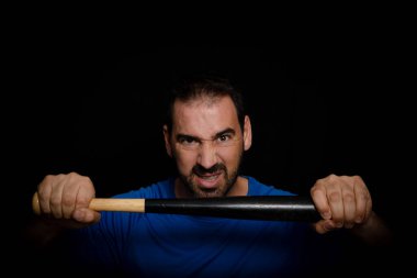 Küstah pozu veren mavi tişörtlü sakallı adam siyah bir arka planda beyzbol sopasıyla poz veriyor. Tehdit konsepti.