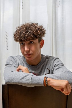 Beyaz perde arkasında gri kazak giyen kıvırcık saçlı çekici genç adam. Moda konsepti