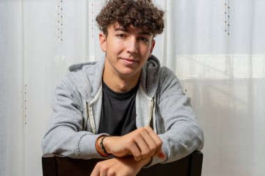 Beyaz perde arkasında gri kazak giyen kıvırcık saçlı çekici genç adam. Moda konsepti