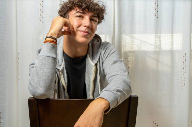 Beyaz perde arkasında gri kazak giyen kıvırcık saçlı çekici genç adam. Moda konsepti