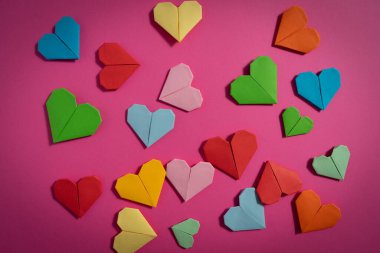 Sevgililer Günü 'nde birbirlerine aşık çiftler için pembe arka planda renkli kağıtlardan yapılmış Origami kalpleri. Aşk konsepti