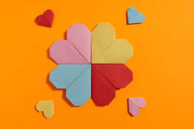 Sevgililer Günü 'nde turuncu arka planda aşık çiftler için renkli kağıtlardan yapılmış Origami kalpleri. Aşk konsepti