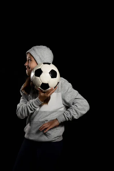 穿着灰色运动衫的小女孩和两个小辫子在玩一个被黑色背景隔开的足球 体育概念 — 图库照片