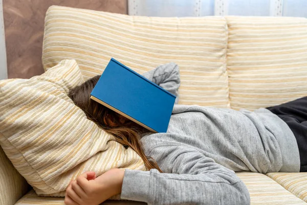 Cute little girl napping with a book she has just read on the sofa in her living room. Selective focus. Rest concept.