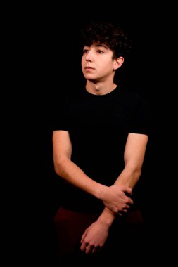 Siyah arka planda poz veren kıvırcık saçlı çekici bir genç. Moda konsepti