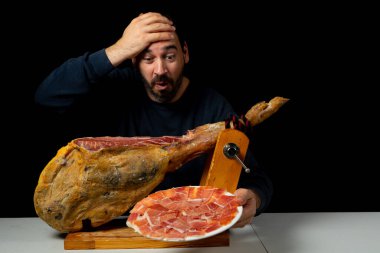 Elinde jambon bıçağı olan sakallı bir adam siyah stüdyo arka planında izole edilmiş tipik bir İspanyol jambonu kesmeye hazır. Süper yiyecekler. Lezzetli aperatif. Besleme kavramı