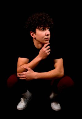 Siyah arka planda poz veren kıvırcık saçlı çekici bir genç. Moda konsepti