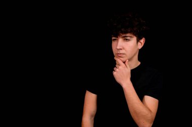 Siyah arka planda poz veren kıvırcık saçlı çekici bir genç. Moda konsepti