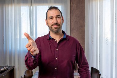 Mor gömlekli İspanyol yakışıklı adam beyaz perdelerle arka plandaki oturma odasında poz veriyor ve el kol hareketi yapıyor. Hareketli kavram