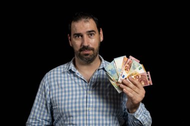 Ekose gömlekli sakallı bir adam bir elinde siyah stüdyo arka planında izole edilmiş euro banknotları tutuyor. Kâr kavramı