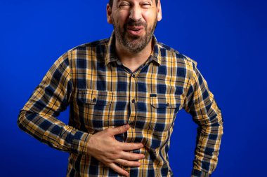 Mavi arka planda karnı ağrıyan İspanyol bir adam, sağlık konsepti.