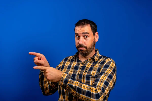 Homem elegante em camisa xadrez mostra os dedos para o lado em um fundo azul Espaço Copiar — Fotografia de Stock