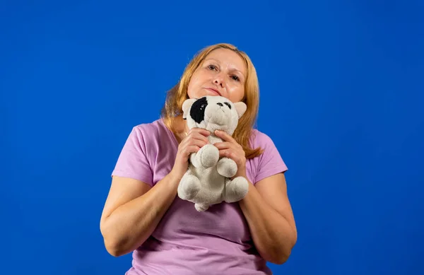 Милая женщина средних лет играет с плюшевым щенком на синем фоне студии. — стоковое фото
