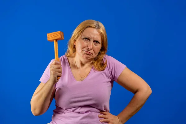 Bella donna di mezza età in posa con un martello di legno cucina isolato su sfondo blu studio. — Foto Stock