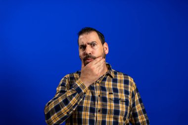 Yakışıklı, orta yaşlı, gri saçlı, soyutlanmış mavi arka planı olan, eli çenesinde soru soran, düşünceli bir adam. Gülen ve düşünceli bir yüz. Şüphe kavramı.