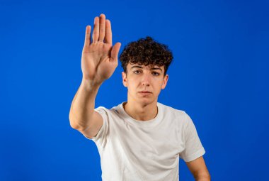 Beyaz tişörtlü beyaz tenli yakışıklı adam mavi arka planda ciddi ve avuç içiyle şarkı söylemeyi kesiyor. Mavi stüdyo arka planında izole edilmiş. İsyancı kavramı