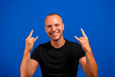 Mavi arka planda siyah tişörtlü, beyaz, yakışıklı genç bir adam çılgın bir ifadeyle el kaldırarak rock sembolü yapıyor. Müzik yıldızı. Ağır müzik konsepti