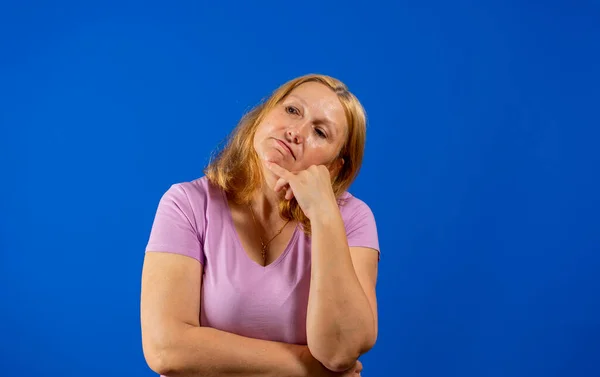 Латиноамериканка средних лет изолирована на синем фоне вдумчиво смотрящая на пространство для копирования, прикрывающее рот рукой. — стоковое фото