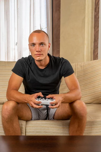 Essa é a minha melhor rotunda.Emocionado jovem homem bonito jogando videogame e mantendo a boca aberta enquanto sentado no sofá em casa. Conceito de jogo — Fotografia de Stock