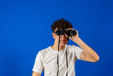 Genç adam mavi arka planda ve uzaktan dürbünle bakıyor.