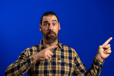 Mavi arka planda, genç bir adamın parmak göstererek biriyle tartışırken yan görüntüsü..