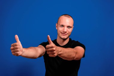 Mavi gözlü, mavi gözlü, onaylı genç beyaz adam mavi stüdyo arka planında izole bir şekilde baş parmağını kaldırıyor. Onaylama kavramı