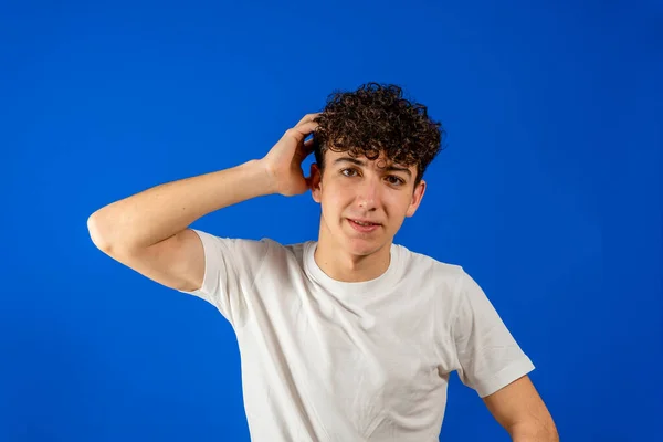 Jonge blanke knappe man met krullend haar over blauwe achtergrond die lijdt aan hoofdpijn wanhopig en gestrest omdat pijn en migraine. Handen op het hoofd. — Stockfoto