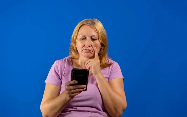 Средняя женщина на изолированном синем фоне думает и отправляет сообщение — стоковое фото