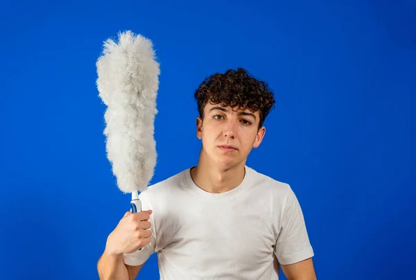 Beyaz bir genç, mavi stüdyo arka planında temizlik tozuyla komik poz veriyor. Temizlik kavramı — Stok fotoğraf