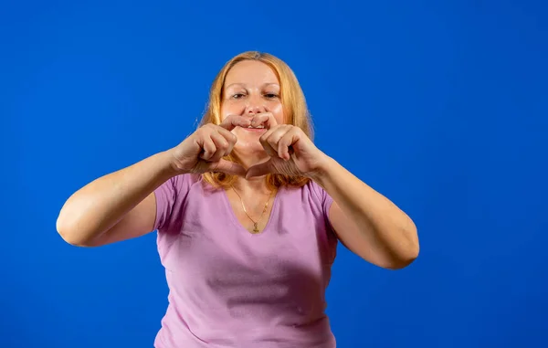 Красивая женщина средних лет в повседневной рубашке фиолетовый на изолированном голубом фоне улыбаясь в любви делает сердце символа формы с руками. — стоковое фото