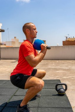 Kafkasyalı genç adam sokakta çan ağırlıklarıyla çömeliyor forma girmek ve vücudu hakkında iyi hissetmek için antrenman yapıyor. Sağlıklı yaşam konsepti
