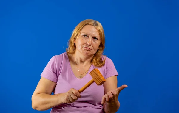 Bella donna di mezza età in posa con un martello di legno cucina isolato su sfondo blu studio. — Foto Stock