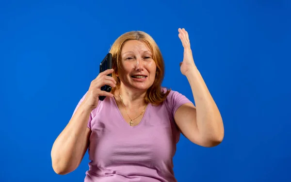 Mittelblonde Frau, die auf Smartphone über blauem, isoliertem Hintergrund spricht, gestresst mit der Hand auf dem Kopf, schockiert vor Scham und Überraschung, wütend und frustriert. Angst und Verärgerung über Fehler. — Stockfoto