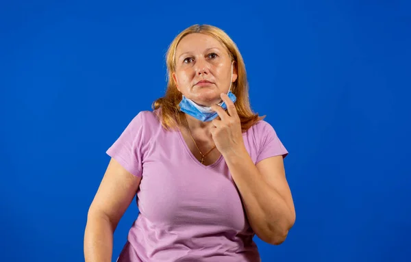 Средняя блондинка снимает медицинскую маску на голубом фоне — стоковое фото