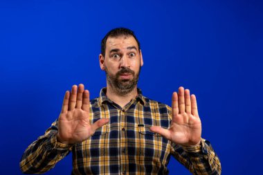 Ne mutlu ekose gömlekli neşeli bir adam ağzını kocaman açtı ve mavi arka planda avuçlarını gösterdi.