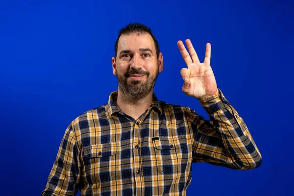 Mladý šťastný muž zvedne ruku a mávne rukou na znamení "ok", na modrém pozadí — Stock fotografie