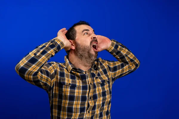 Joven hombre guapo con camisa a cuadros casual de pie sobre fondo azul aislado Loco y asustado con las manos en la cabeza, asustado y sorprendido de shock con la boca abierta — Foto de Stock