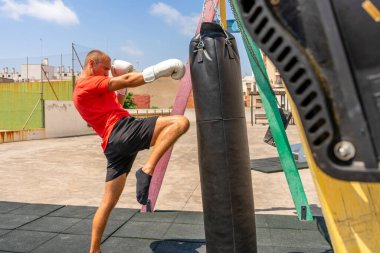 Spor elbiseli, kendinden emin genç bir adam dışarıda egzersiz yaparken kum torbasını tekmeliyor. Eğitim kavramı