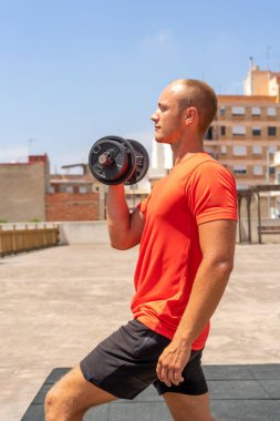 Yakışıklı kaslı adamın dikey çekimi dışarıda ağırlık kaldırıyor ağırlık kaldırma antrenmanına hazırlanıyor, kaslı kolları var, sokak arka planında poz veriyor. Güç gelişiyor.