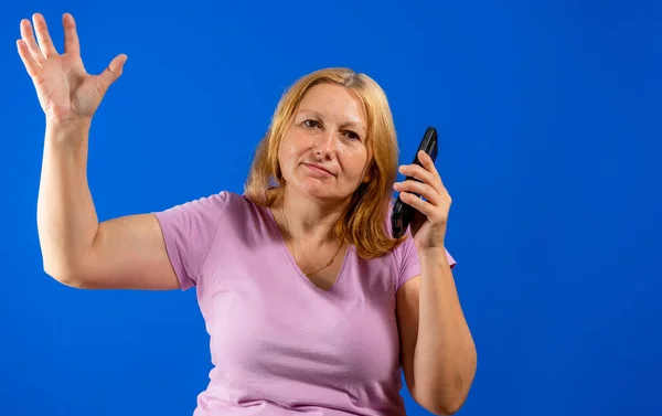 Средняя блондинка, говорящая на смартфоне на синем изолированном фоне, напряженная рукой на голове, шокированная стыдом и удивлением, сердитая и расстроенная. Страх и разочарование по ошибке. — стоковое фото