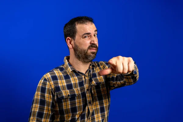 Jovem homem bonito vestindo camisa xadrez casual em pé sobre fundo azul isolado alegre com um sorriso no rosto apontando com a mão e o dedo até o lado com expressão feliz e natural — Fotografia de Stock